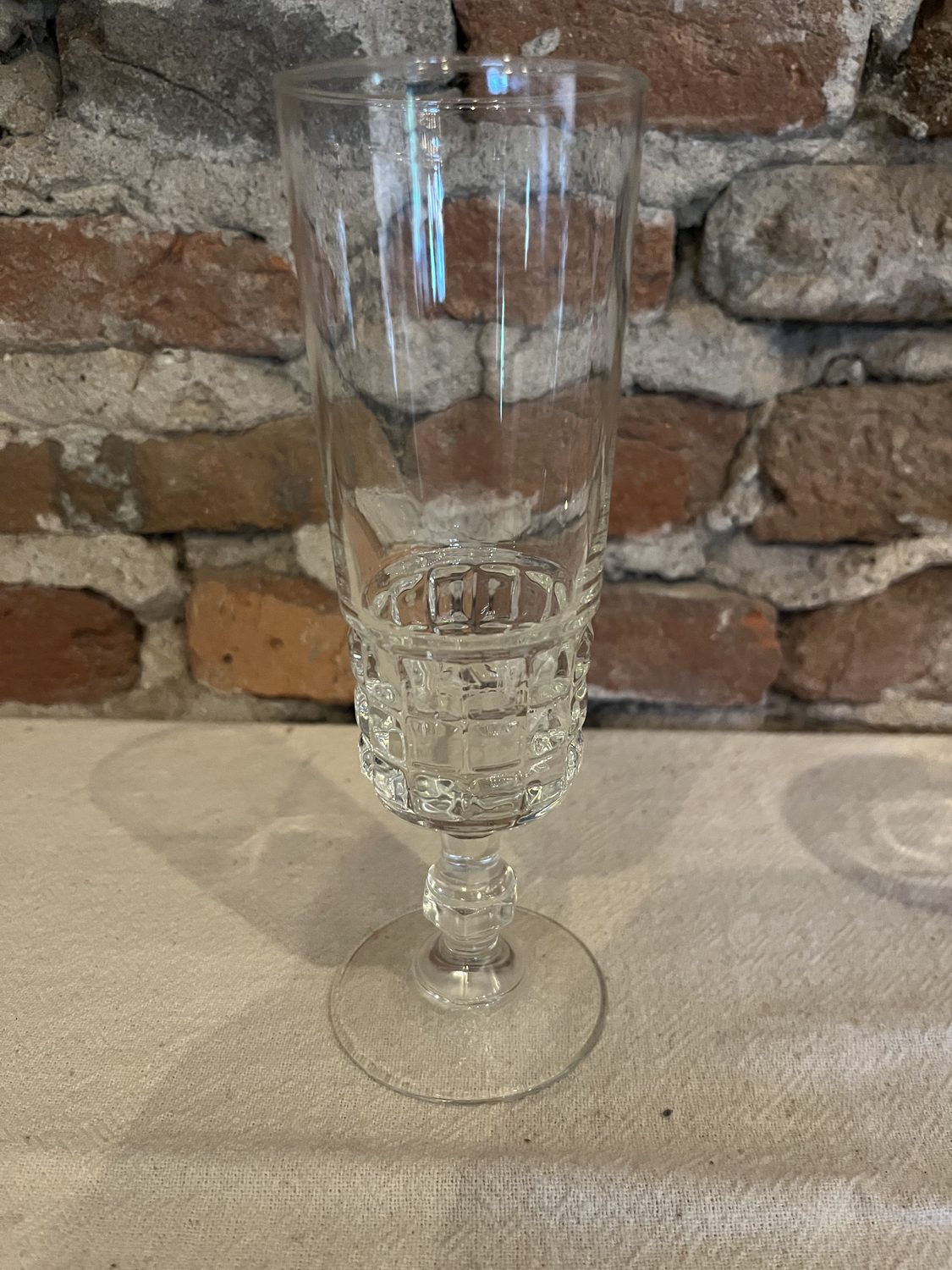 Hoog champagneglas op voet met een geslepen blokjesmotief, voor een bakstenen muur