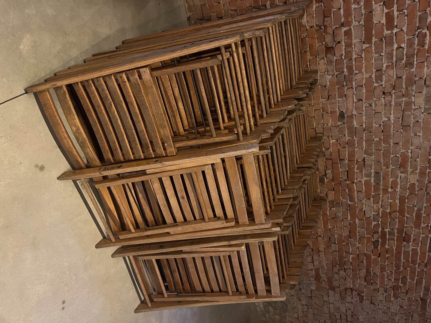 Stapels dichtgeklapte houten stoelen tegen een bakstenen muur in de schuur